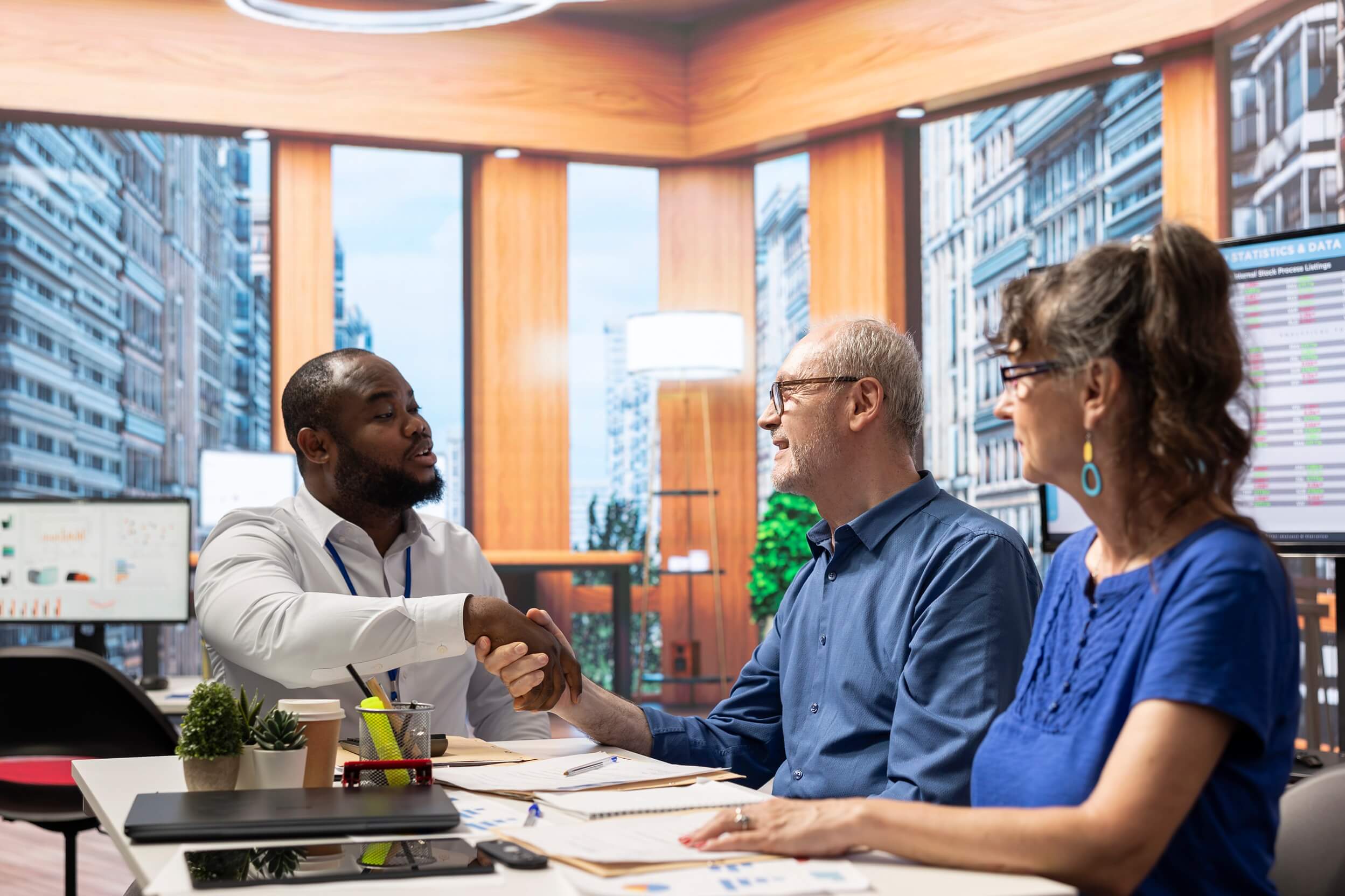 Three people shaking hands at a meeting table, representing collaboration at Innovation Behavior Services.