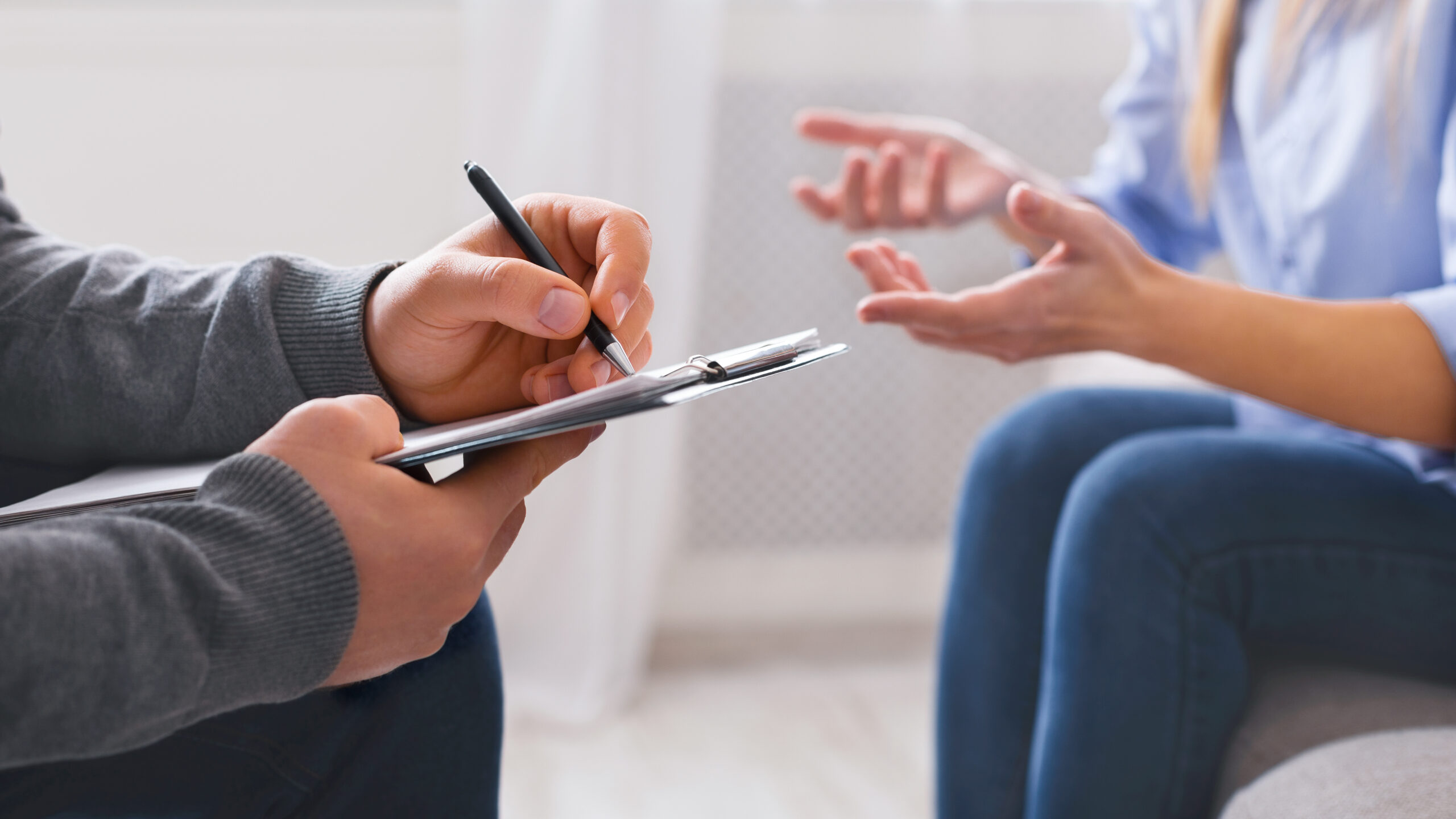 Therapeutic consultation session with a professional taking notes while a client shares concerns.